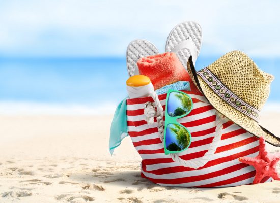 Summer vacations concept background. Beach bag, straw hat, flip flops, sunglasses and starfish on sandy beach and azure sea on background.
